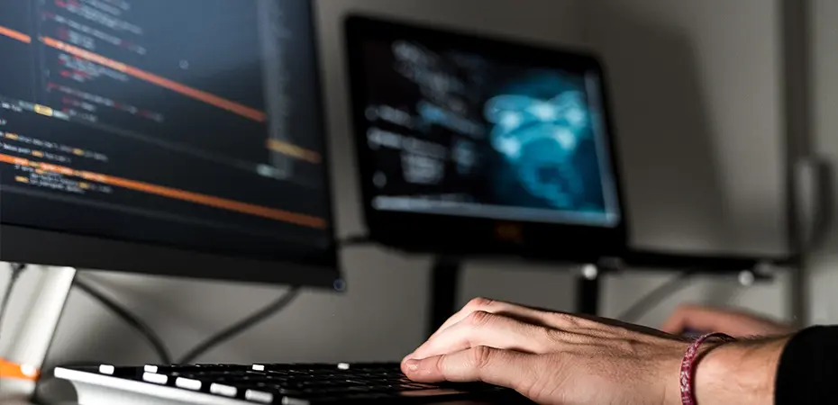 Close up of hands typing on keyboard with screens in the background.