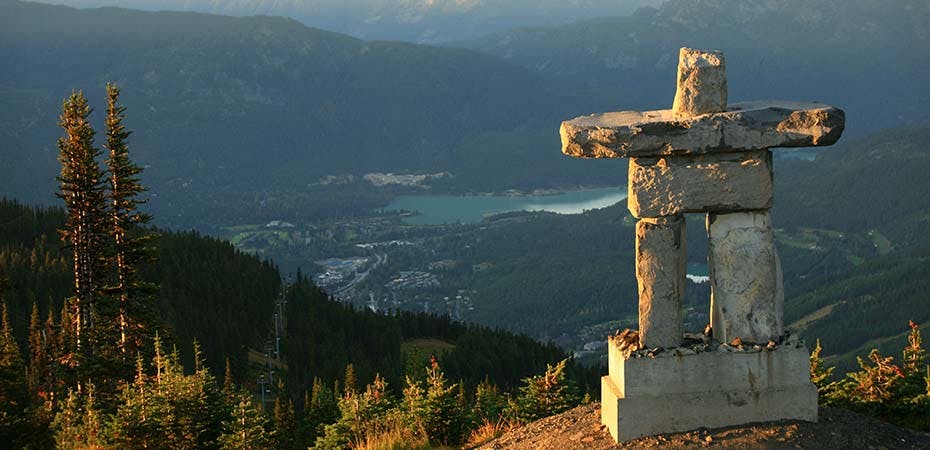 An inukshuk in Whistler, BC, Canada. This beautiful inukshuk - a rock statue that was symbolic for First Nations people - stands at the top of Whistler Mountain in the Whistler Blackcomb Resort in Whistler, British Columbia, Canada. The image was taken in summer. Coast Mountains in background. Nobody is in the image.