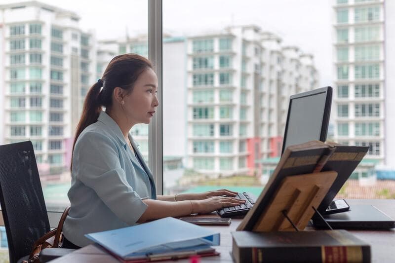 Lawyer office, Asian female barrister typing on keyboard, preparing legal document and getting reference from law books