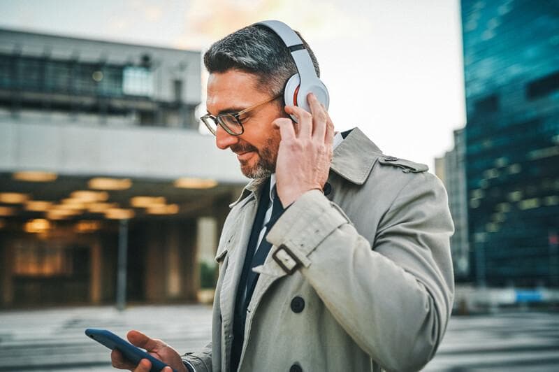 Shot of a mature businessman wearing headphones and using a cellphone in the city